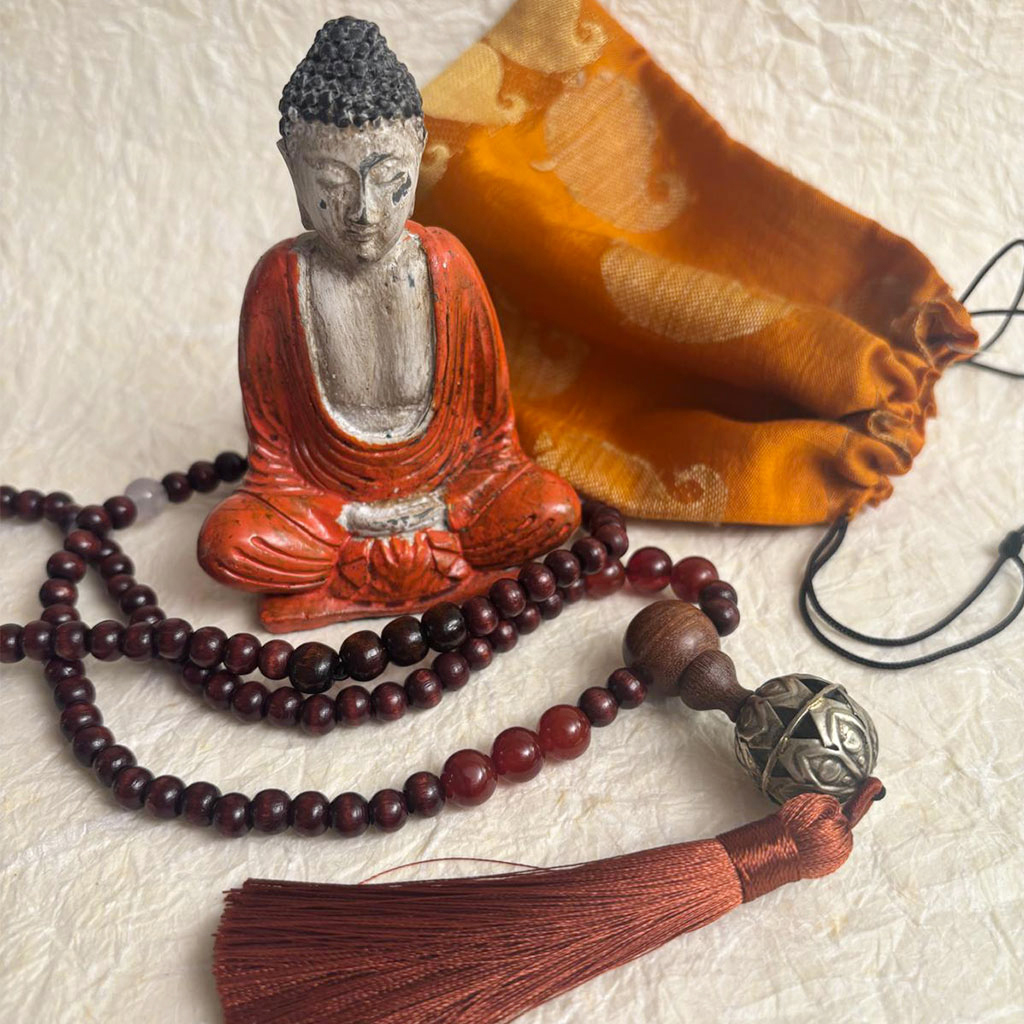 Piccolo Budda in resina con Japamala in legno di rosa e corniola, nappa in cotone e sacchetto arancione in seta di sari indiano.